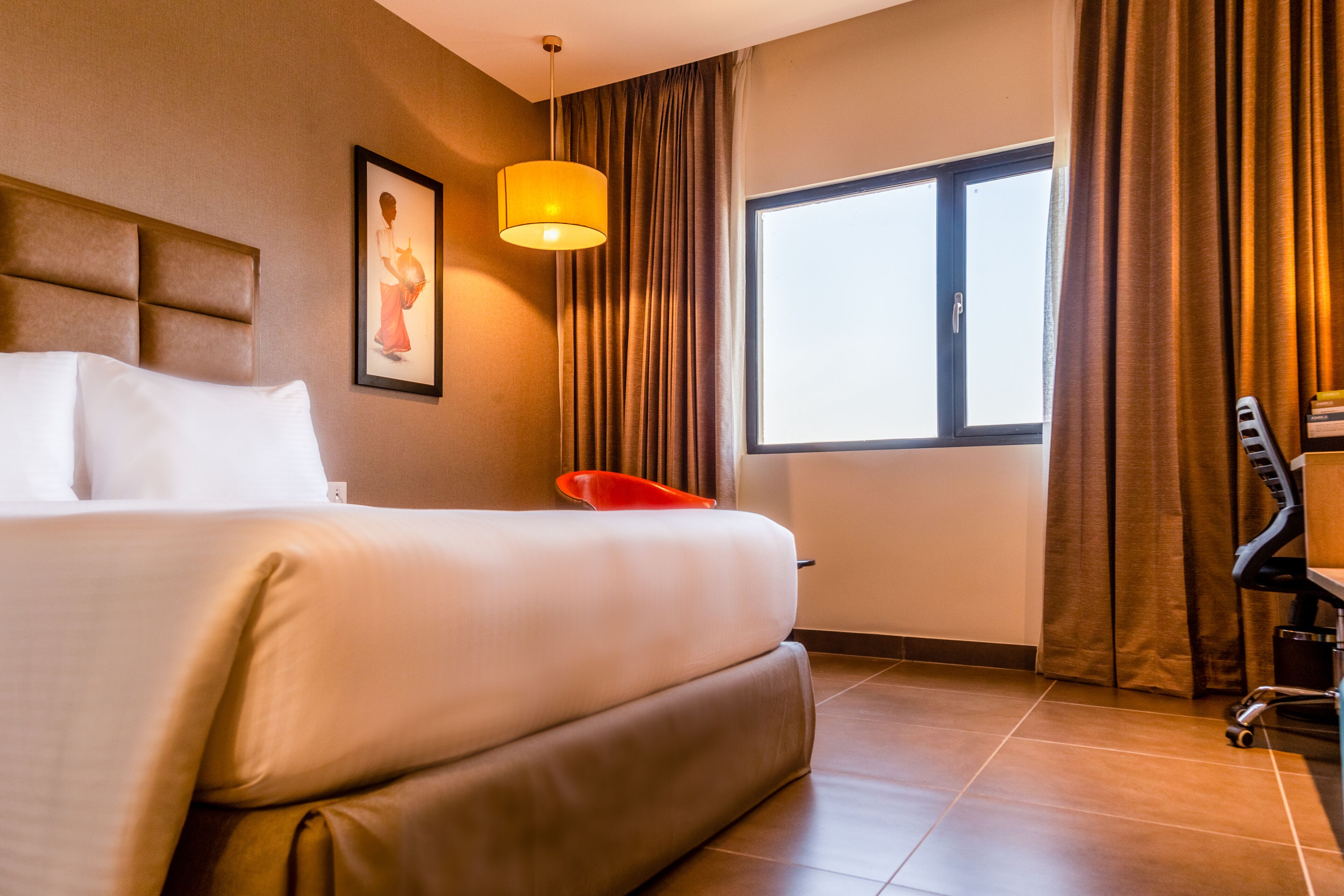 Habitación de hotel con una cama grande, un escritorio, una silla, una ventana y un cuadro en la pared.