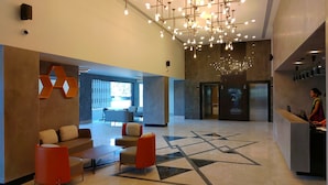 Un vestíbulo moderno con suelo de diseño geométrico, un mostrador de recepción y una zona de estar con sillas naranjas.