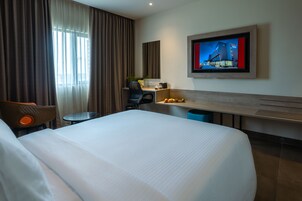 Une chambre d’hôtel avec un grand lit, un bureau avec une chaise, un téléviseur fixé au mur et une fenêtre avec des rideaux.