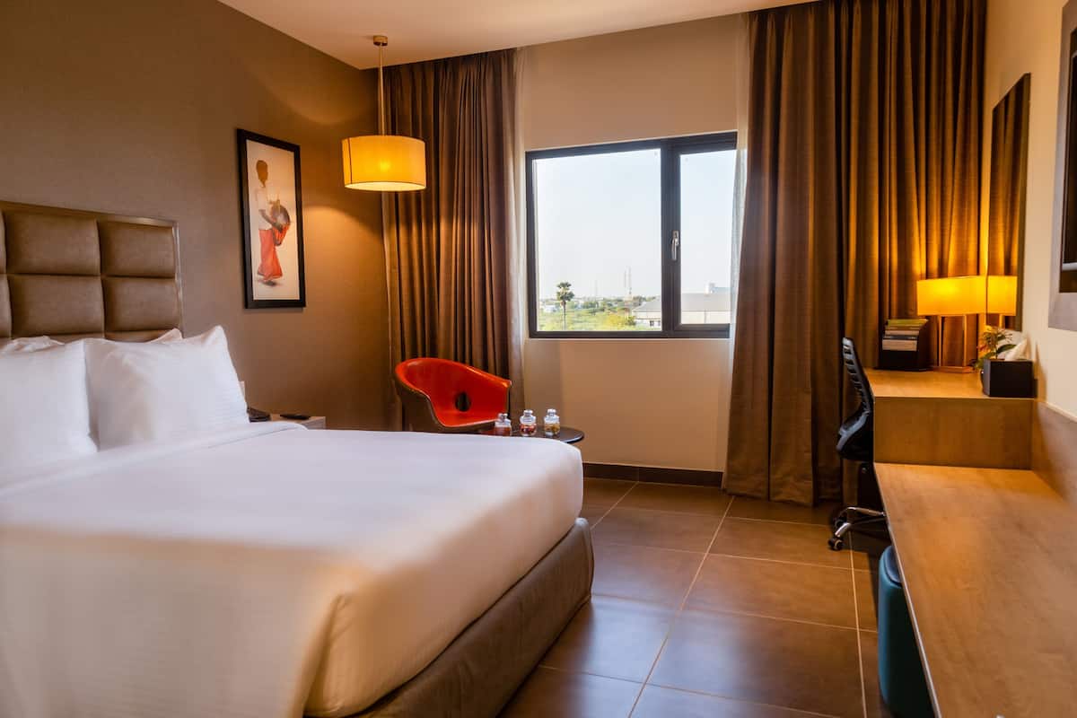 Une chambre d’hôtel avec un grand lit, un bureau, une chaise, une fenêtre avec des rideaux et un tableau au mur.