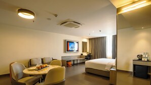Habitación de hotel con cama, escritorio, silla, mesa con frutas, televisor y cafetera.
