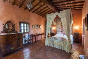 Ein Schlafzimmer mit Himmelbett, Holzkommode und Schreibtisch mit Stuhl.