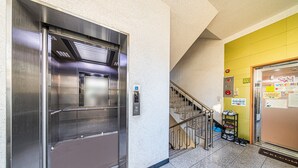 An elevator with a metallic finish, a staircase with metal railings, and a yellow wall with a welcome sign. - Dream Single House (Seoul)
