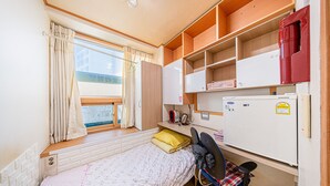 A compact room with a single bed, a desk with a chair, a small window with curtains, and a white refrigerator. - Dream Single House (Seoul)