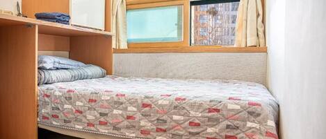 Una habitación pequeña con cama, un estante y una ventana.