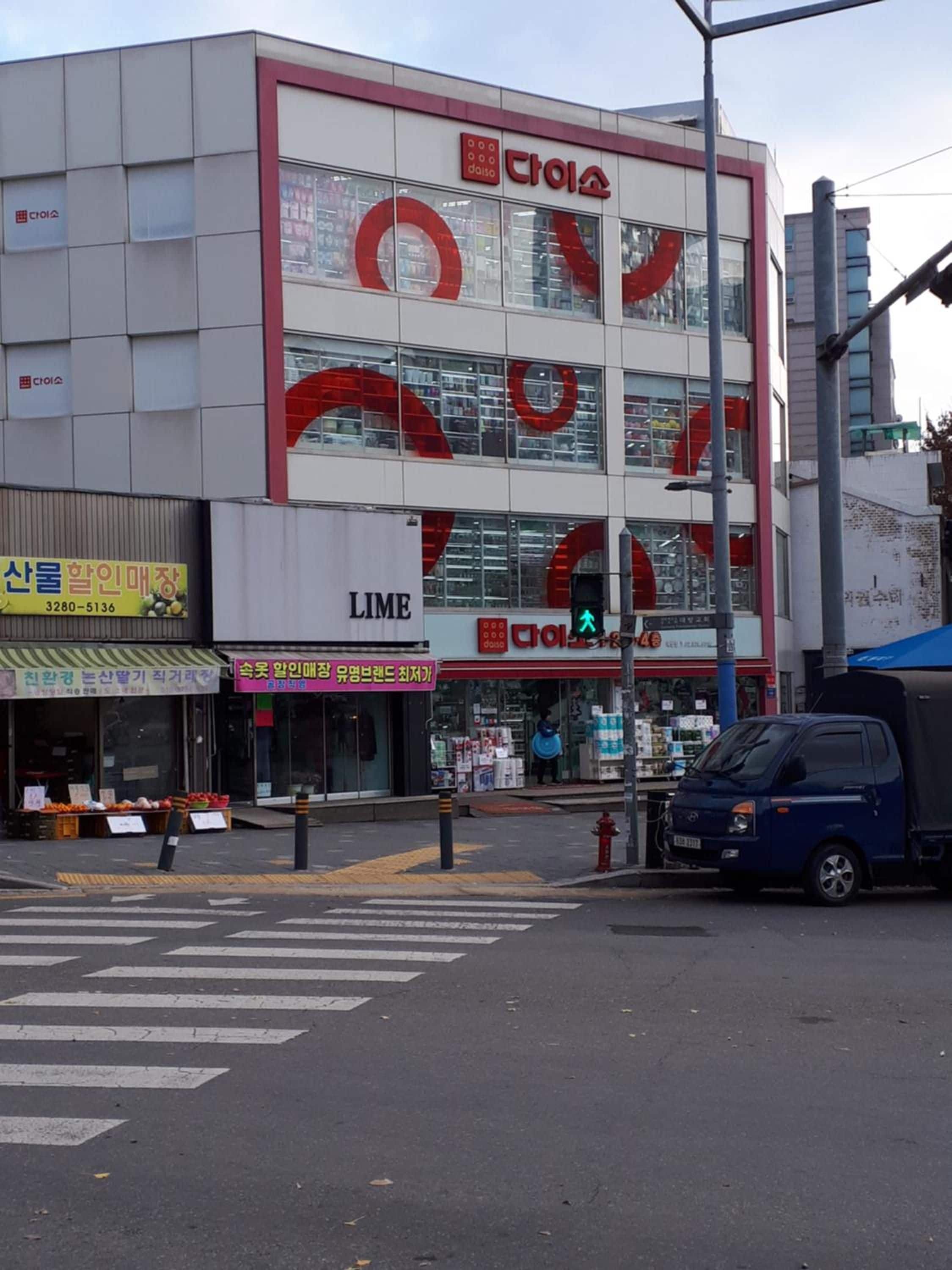 A multi-story building with a prominent red and white logo, a visible storefront with a sign, and a crosswalk in front.