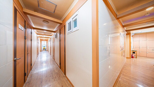A long, narrow hallway with wooden doors and tiled walls, leading to a room with wooden cabinets. - Dream Single House (Seoul)