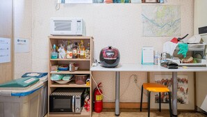 A compact kitchen with a microwave, shelves with food items, a fire extinguisher, and a calendar on the counter. - Dream Single House (Seoul)