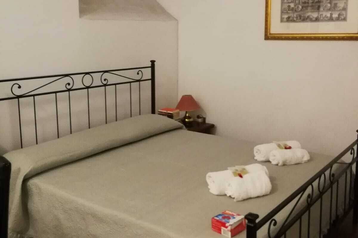 A bedroom with a bed, a nightstand, a framed picture, and a window.