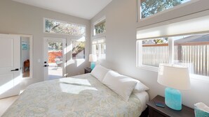 A bedroom with a bed, two bedside tables, a window, and a door leading to a patio.