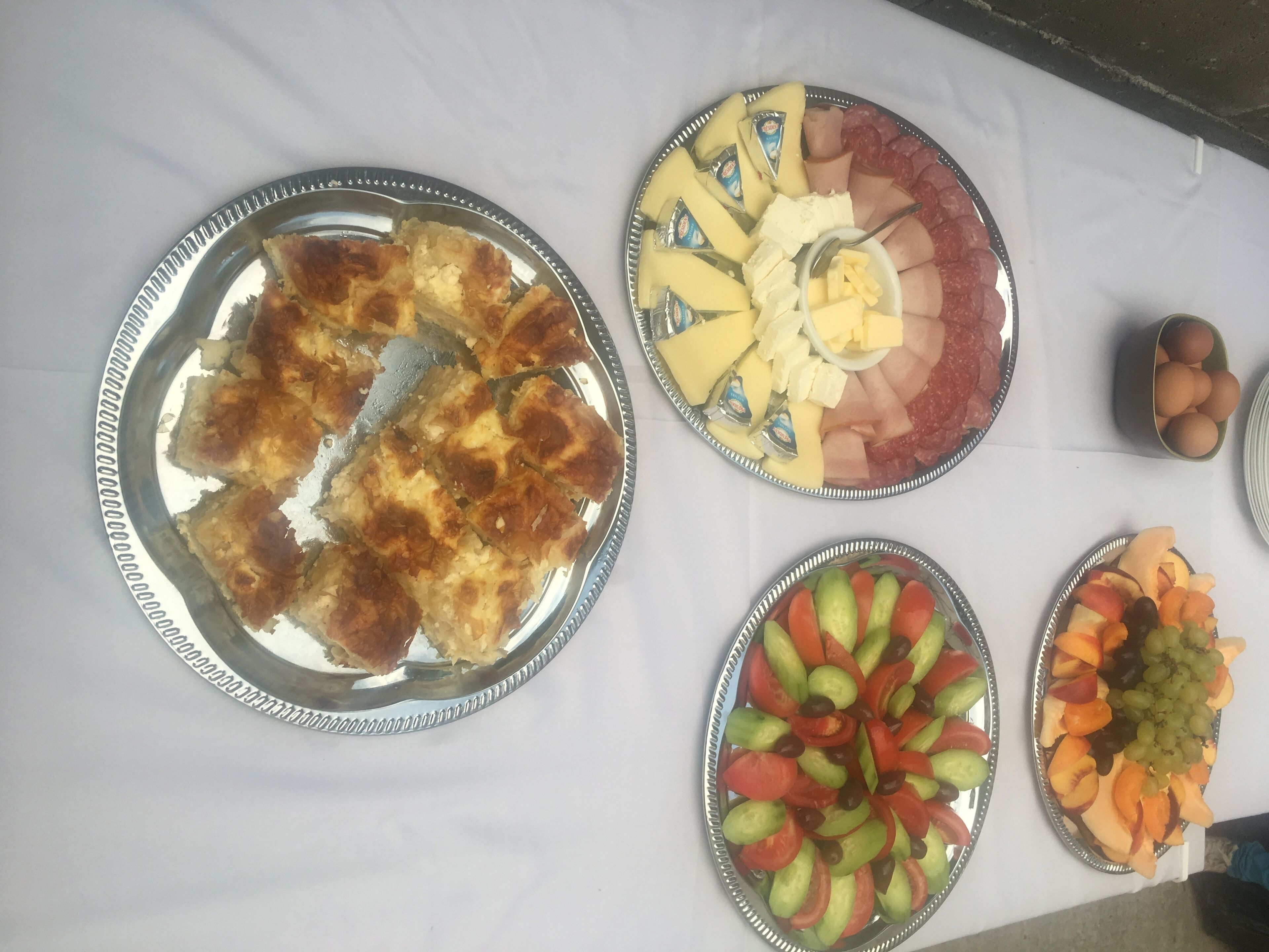 Een tafel met diverse etenswaren, waaronder een bord met sneetjes brood, een schotel met kaas en ham, en een fruitsalade.