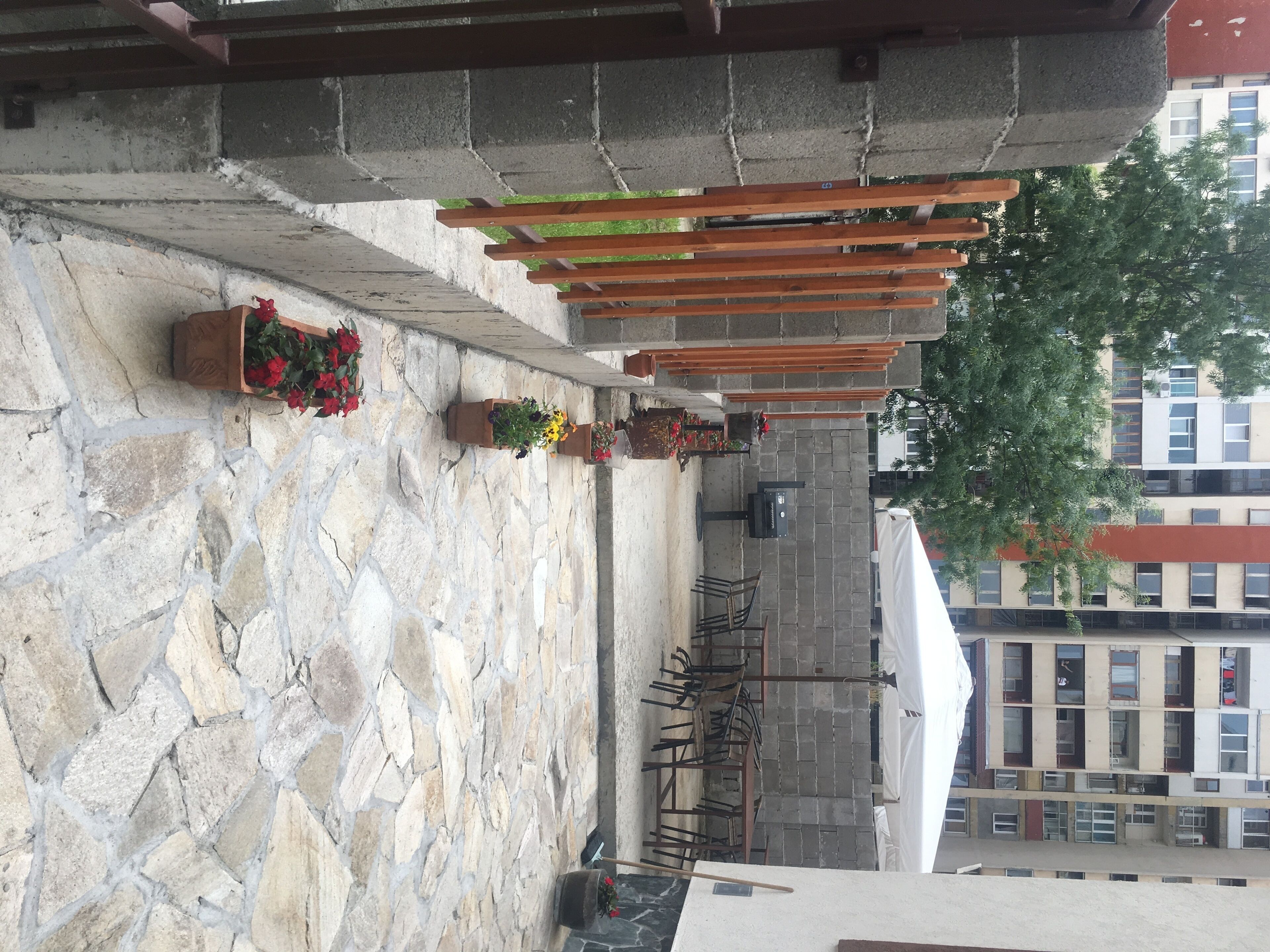 Een erf met stenen bestrating, houten pergola's, potplanten en tuinmeubilair.