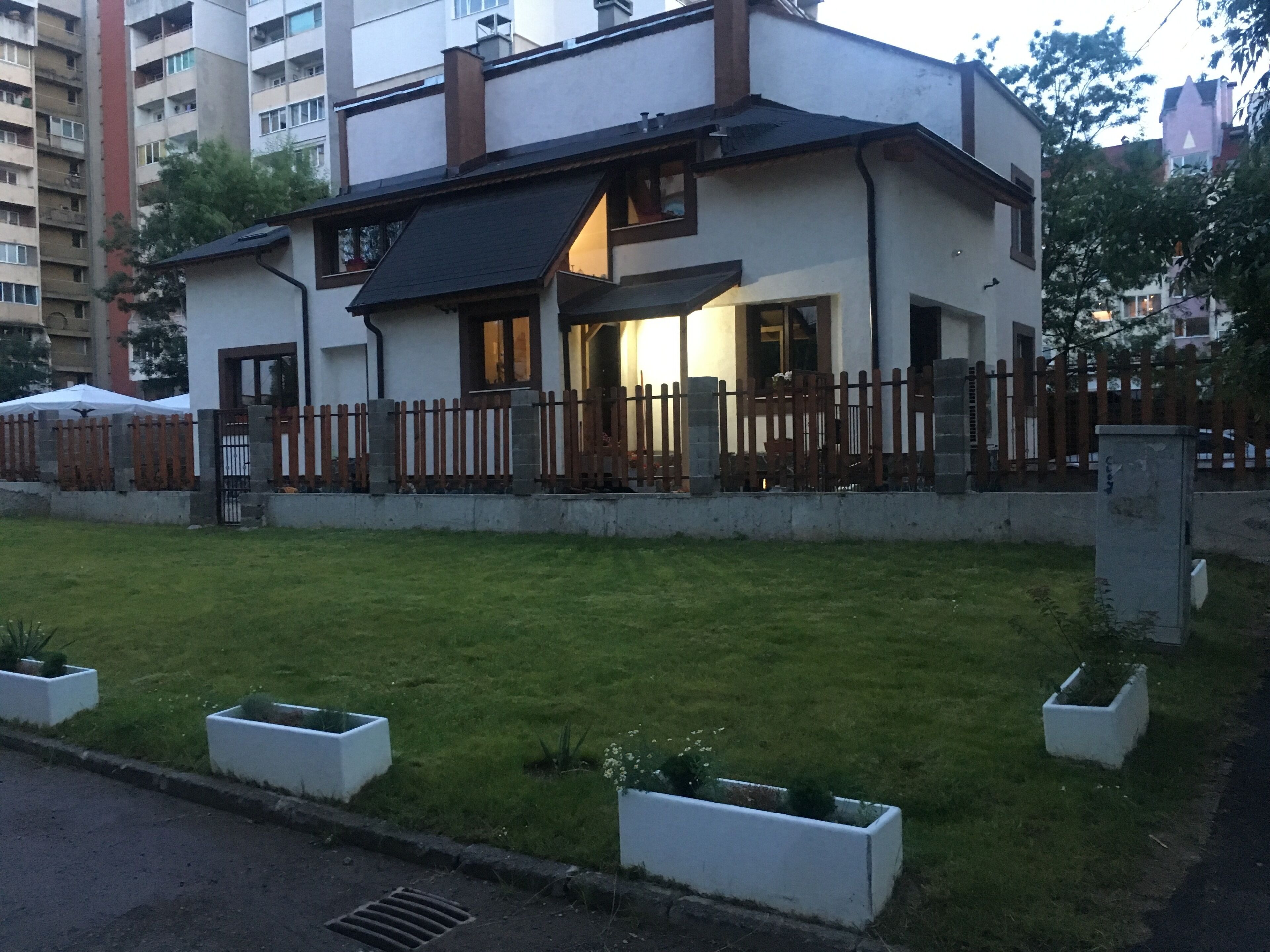 Een gebouw met twee verdiepingen, een plat dak, een houten hek en een verzorgd gazon met plantenbakken.