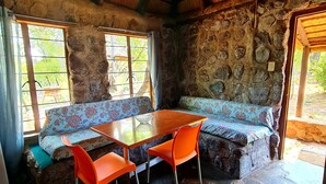 A rustic stone interior with a wooden ceiling, a stone bench, a glass-top table, and orange chairs. - Uitvlugt Resort (Bela-Bela)