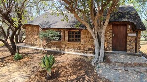 A rustic stone building with a thatched roof, surrounded by trees and a small garden. - Uitvlugt Resort (Bela-Bela)