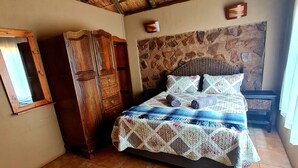 A bedroom with a bed, a wardrobe, a stone wall, and a tiled floor. - Uitvlugt Resort (Bela-Bela)