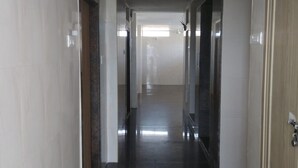 Un pasillo largo y estrecho con piso oscuro y paredes claras, que conduce a una habitación luminosa al final.