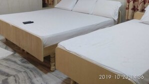 Habitación de hotel con dos camas individuales, cabecera de madera, un control remoto sobre una cama y cortinas con estampado floral.