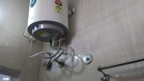 Calentador de agua instalado en una pared con baldosas, con tuberías visibles y un mando metálico.