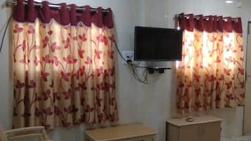 A hotel room with a television mounted on the wall, a wooden chair, a small wooden table, and a cabinet.