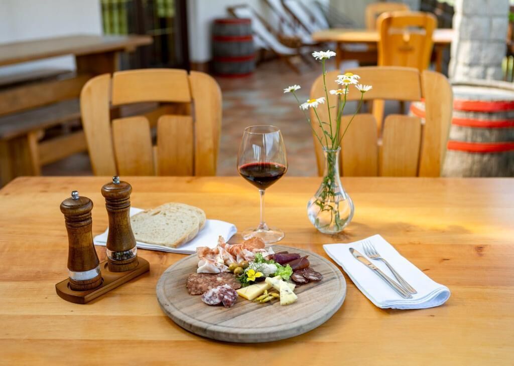 Ein Holztisch mit einer Wurstplatte, einem Glas Rotwein und einer Blumenvase.