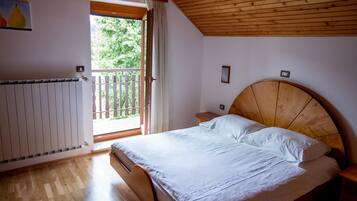 A bedroom with a wooden ceiling, a large bed with white linens, a wooden headboard, a nightstand, a window with a view of greenery, and a radiator on the wall.