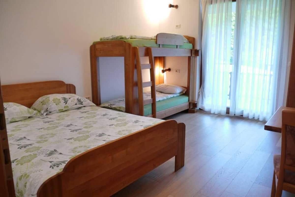 A room with two wooden bunk beds, a wooden desk, and a window with sheer curtains.