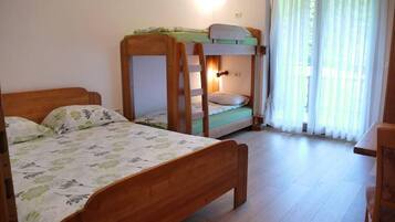 Una habitación con dos literas de madera, un escritorio de madera y una ventana con cortinas translúcidas.
