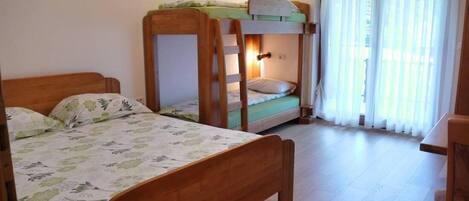 A room with two wooden bunk beds, a wooden desk, and a window with sheer curtains.