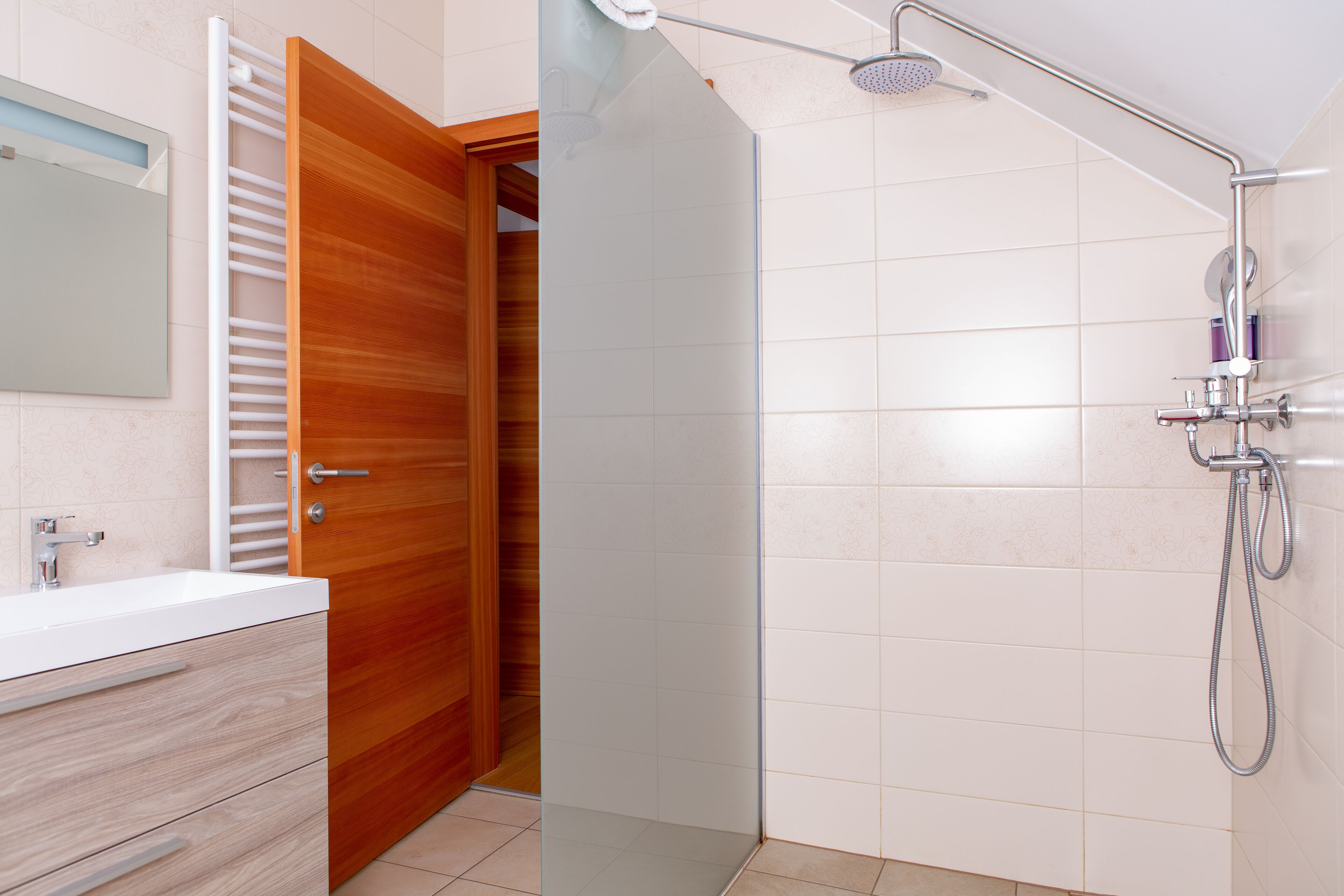 A bathroom with a wooden door, a white sink, and a shower with a handheld showerhead.