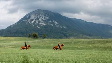Paisagem montanhosa com dois cavaleiros em um campo gramado.