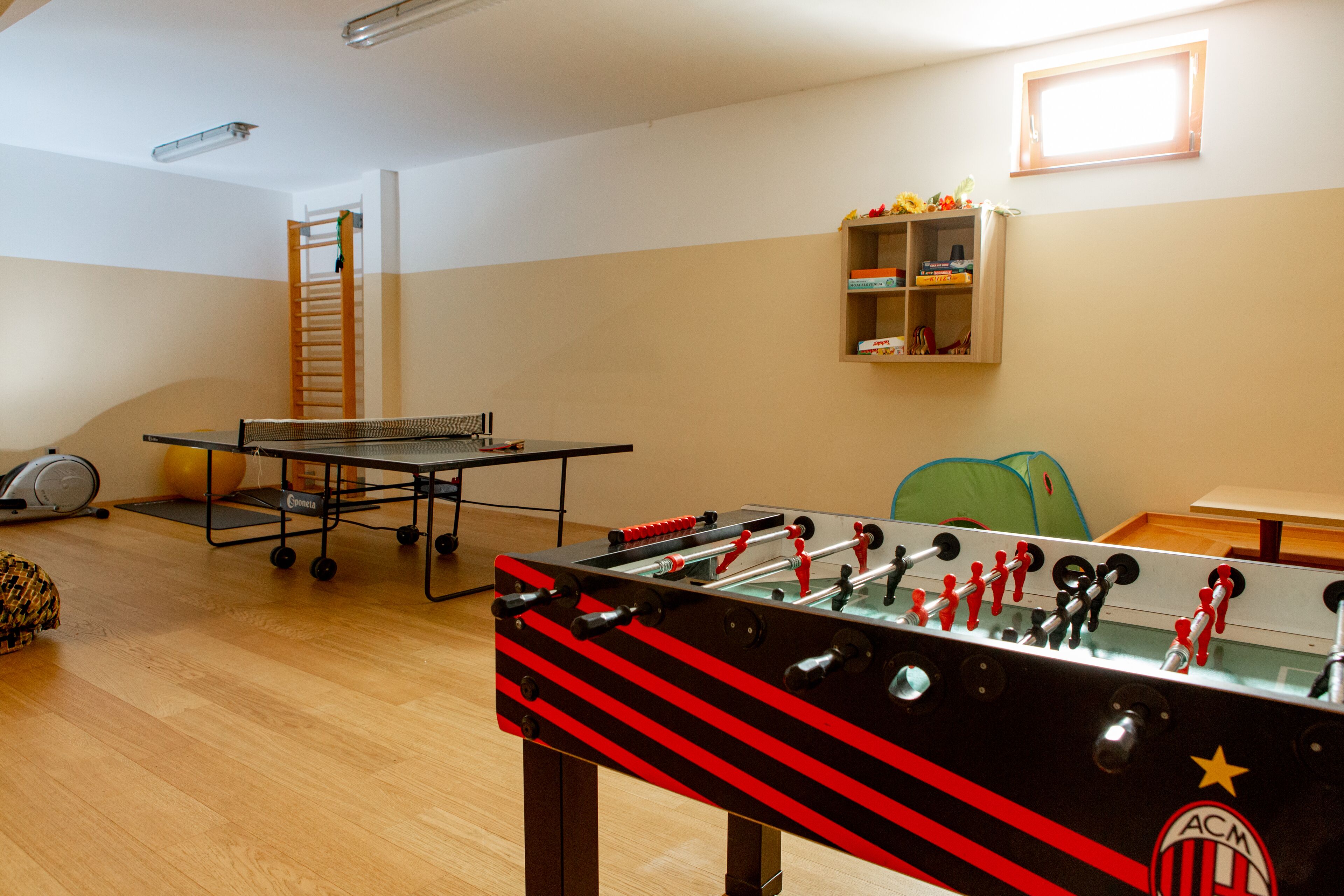 Una habitación con mesa de futbolín, mesa de ping pong, pelota de ejercicios y una escalera.
