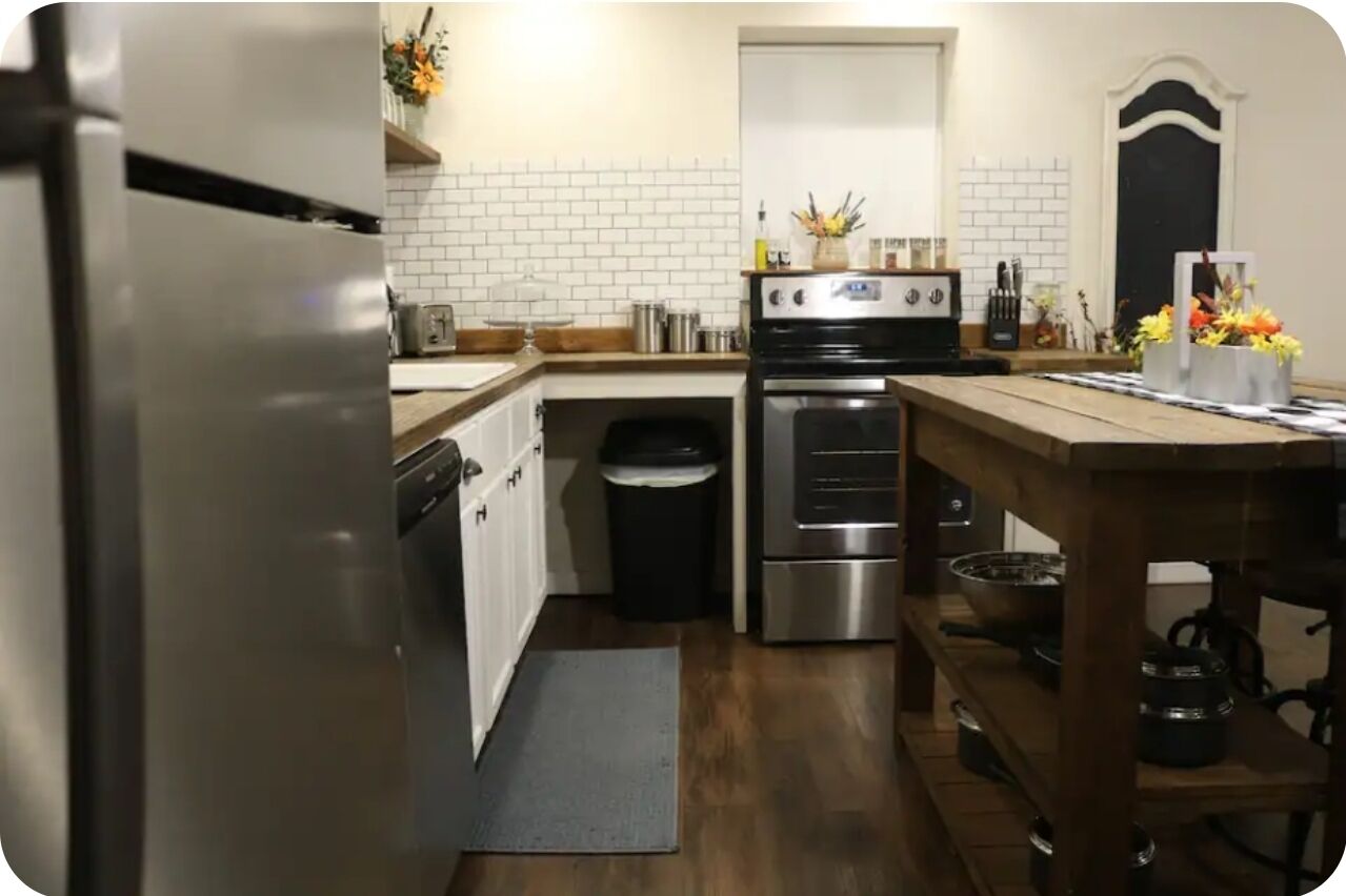 A kitchen with white tiled walls, stainless steel appliances, and wooden flooring.