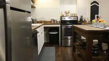 A kitchen with white tiled walls, stainless steel appliances, and wooden flooring.
