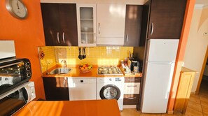Een kleine keuken met een magnetron, broodrooster, gootsteen en een wasmachine.