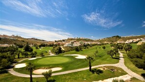Un parcours de golf avec un chemin sinueux, des bunkers de sable et, en arrière-plan, des immeubles résidentiels situés sur une colline.