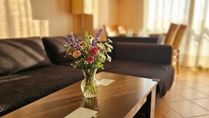 Une pièce avec un canapé marron foncé, une table basse en bois sur laquelle est posé un vase transparent rempli de fleurs, et une lampe à l’arrière-plan.