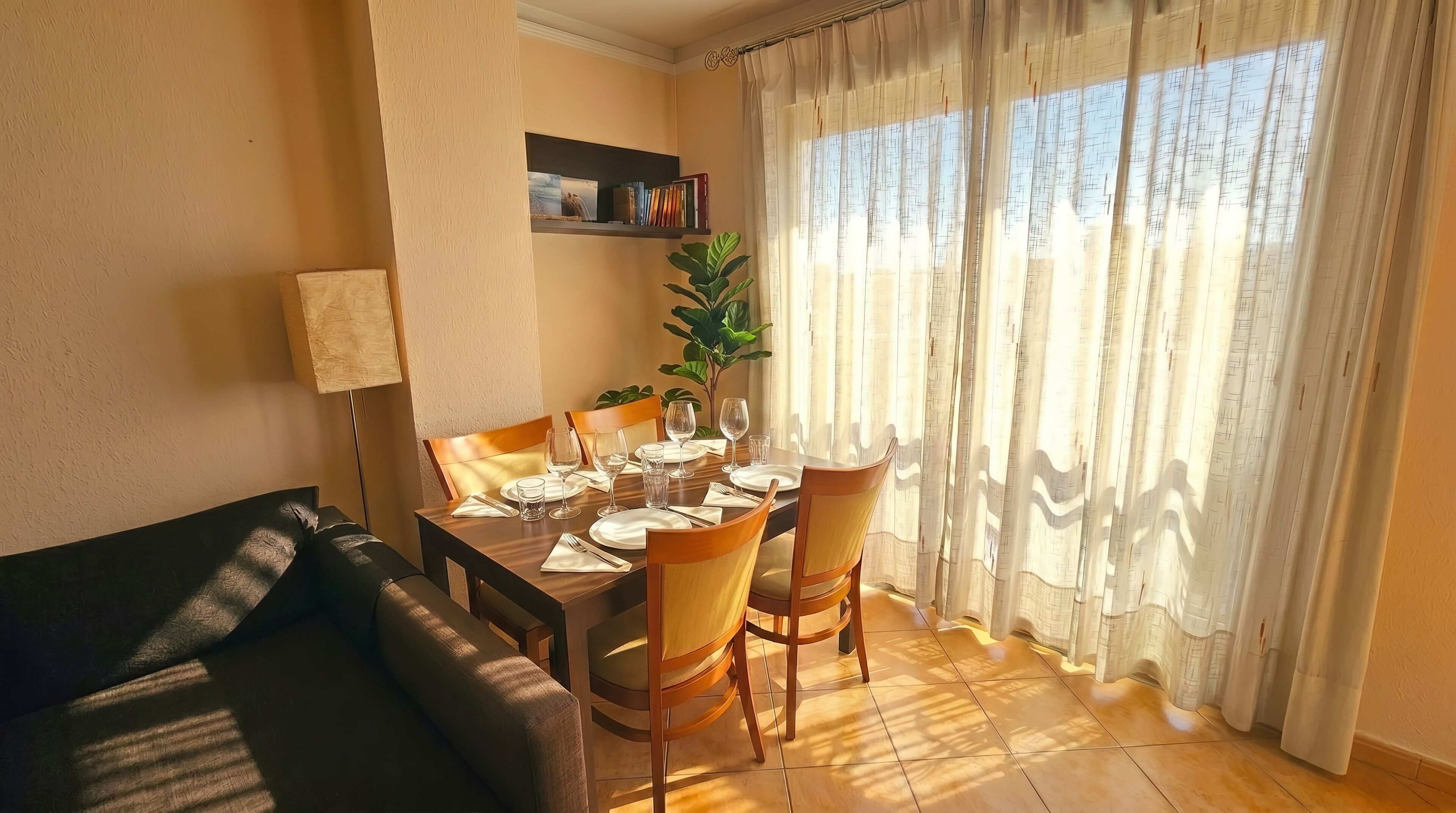 A dining area with a table set for four, chairs, a potted plant, and a bookshelf.