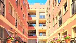 Un couloir au sol carrelé, bordé de bâtiments dotés de balcons et de plantes en pot.