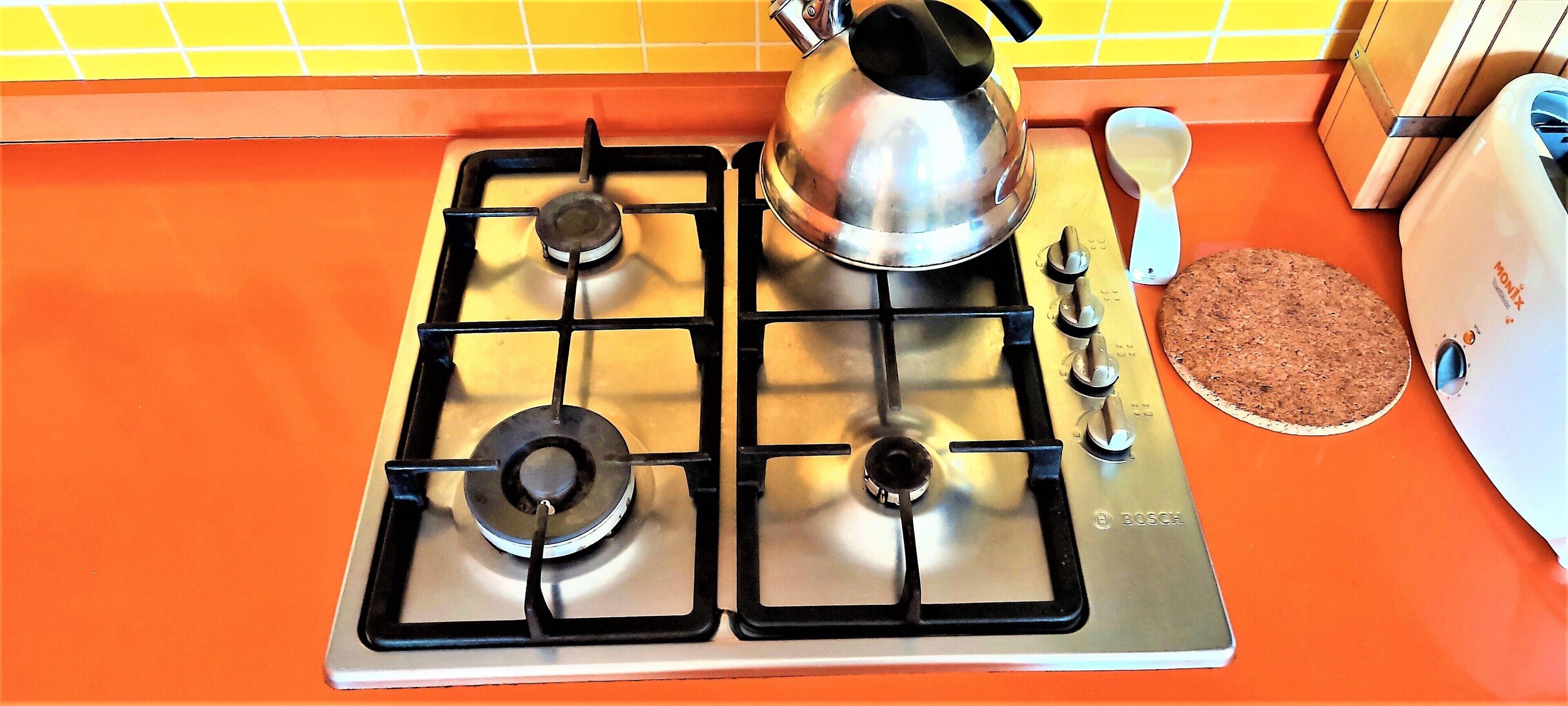Une cuisine équipée d’une cuisinière à gaz, d’une bouilloire, d’un verre doseur et d’un grille-pain.