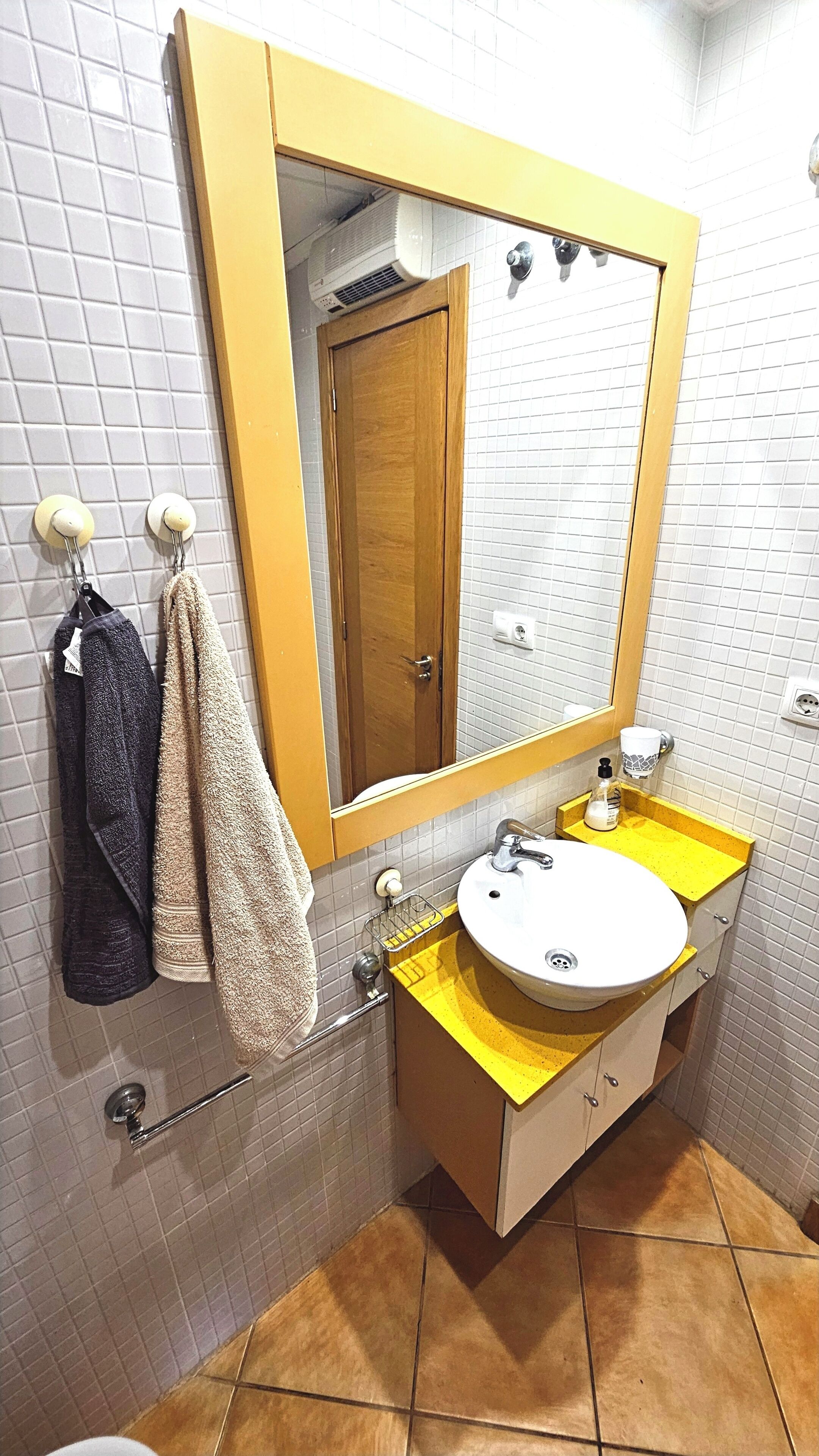 Un baño con un lavamanos amarillo, un espejo, un perchero con toallas y una puerta de madera.