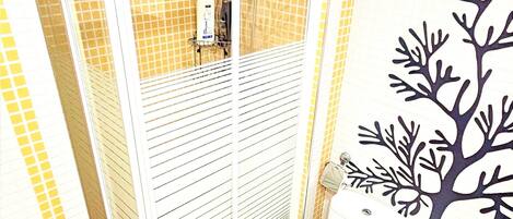 Un baño con cabina de ducha, dos inodoros, un lavabo y un mural decorativo con motivos vegetales.