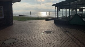 A brick-paved deck with a view of the water, a gazebo, and a brick building. - Apartment Seeweg - your time out in the north (Beverstedt)
