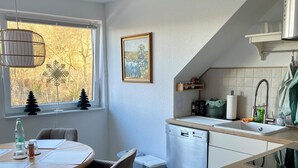A modern kitchen with a dining area, a dishwasher, and a window with a view of trees. - Apartment Seeweg - your time out in the north (Beverstedt)