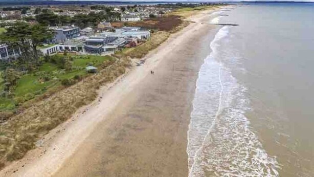 Une vue aérienne d’une zone côtière, avec une plage de sable, une rangée de maisons et une vue dégagée sur l’océan.