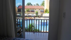 Ein Balkon mit Blick auf einen Pool, ein Bett und eine Ansicht eines Gebäudes mit mehreren Balkonen und Sonnenschirmen.