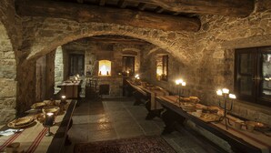 A stone-walled dining hall with a long table set for a meal, candle-lit tables, and a rustic stone ceiling. - Eremito (Parrano)