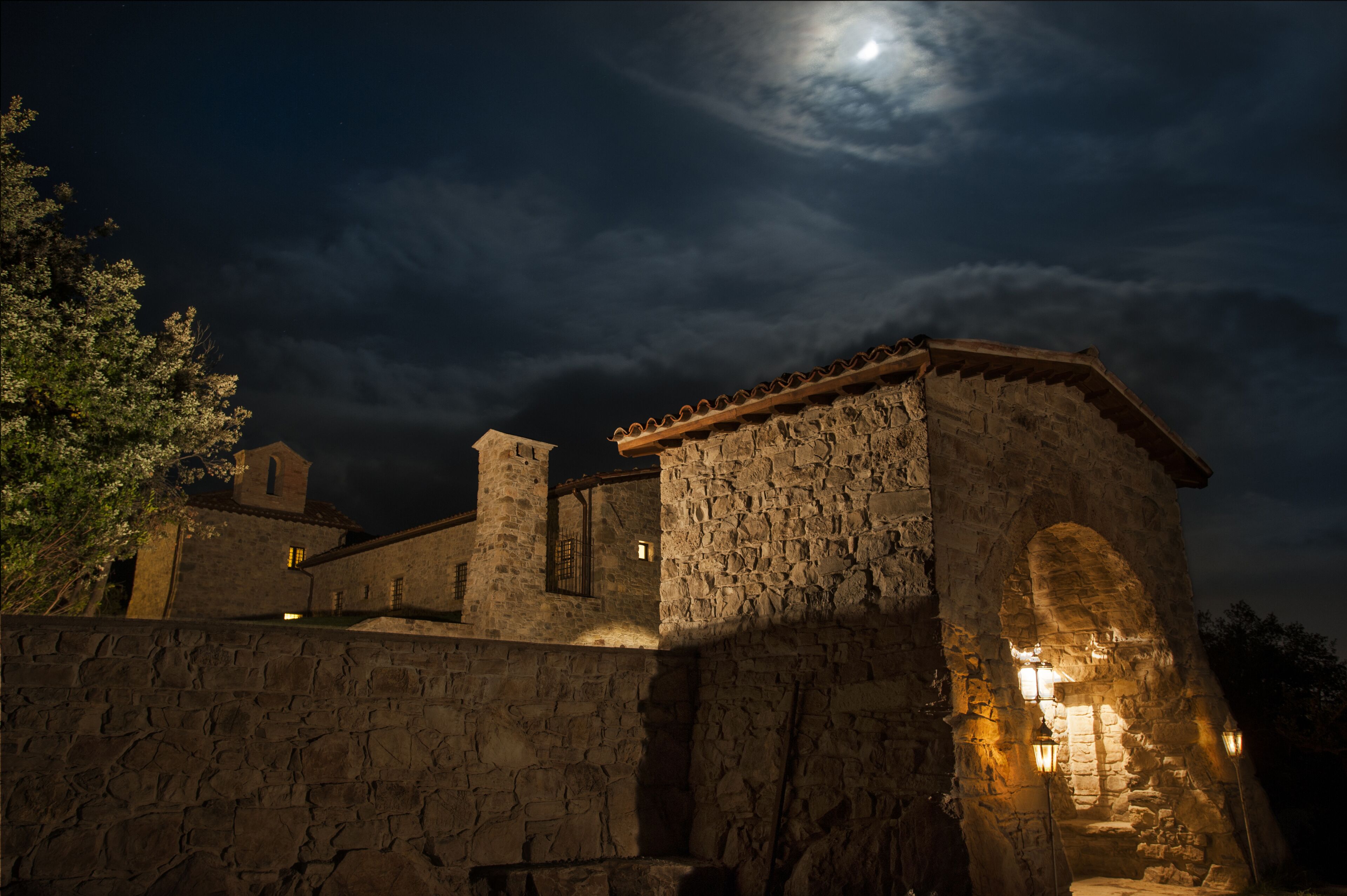 A stone building with a moonlit sky, featuring a prominent archway and a small tower.
