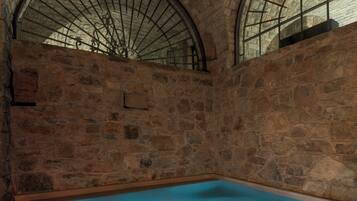 A stone-walled room with a large, rectangular pool and arched windows.