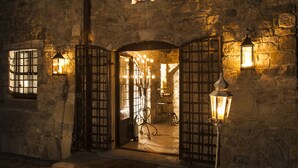A stone building with a large arched entrance, illuminated by wall-mounted lanterns and a central light fixture. - Eremito (Parrano)